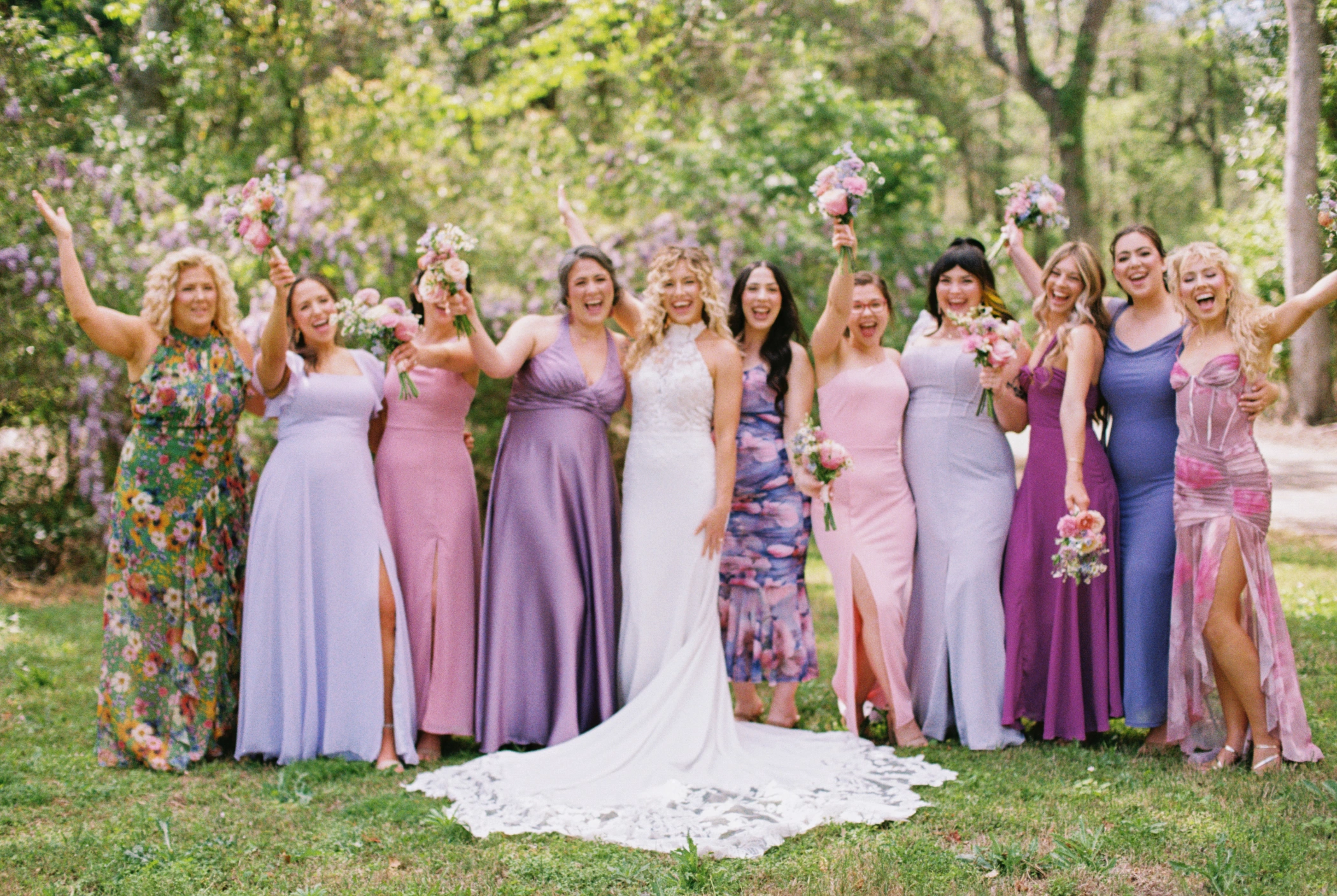 Taylor and her bridesmaids celebrating with bouquets raised, dresses in shades of lavender, pink, and purple