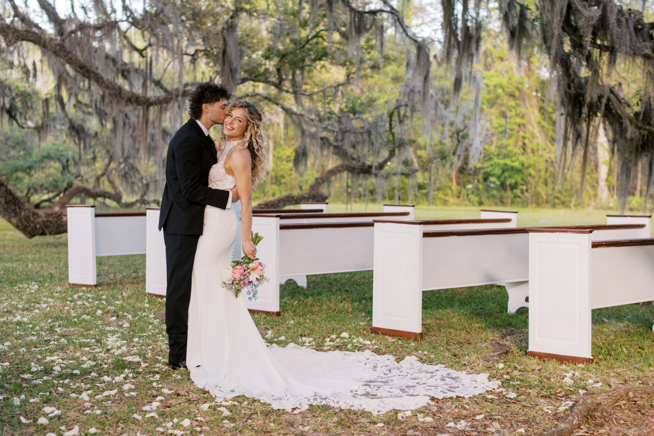Zane kissing Taylor beside the white church pews beneath a massive Spanish moss-draped oak at Keystone Oaks Estate